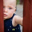 toddler looking intensely through the rungs of a deck