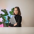 The picture of the article’s author holding a lap-top with a house plant and neon lights in the background.