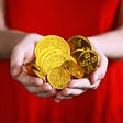 A woman in a red dress is holding gold coins in her hands in front of her.