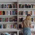 Lady standing at a library bookshelf looking at a book she is curious about