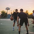 Two people playing basketball outdoors.