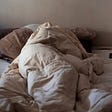 person huddled under covers in bed