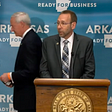 Arkansas Secretary of Health Dr. Nathaniel Smith speaks at a podium as Governor Asa Hutchinson passes behind him.