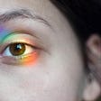 A close-up of a human eye with rainbow light cast over it.