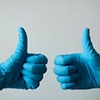 two hands in blue medical gloves giving the thumbs up sign