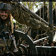 Captain Jack Sparrow standing at helm of what looks to be a grounded Black Pearl, with pirates below looking up at him.