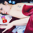 A woman lays on bed with TV static in her eyes, surrounded by logos of social media sites like Instagram, YouTube and Twitter