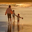 Woman and two children walking on the beach at sunset