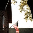 American Flag fluttering in the wind from it’s mast, angled off from a home’s corner.