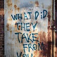 A rusted wall has spray painted on it in blue the handwritten words “What did they take from you?”