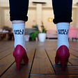 the backs of someone’s feet, wearing white socks that read ‘girls rule’ and a pair of red high heel shoes