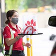 A Chick-fil-A employee delivering food to a drive-thru customer.