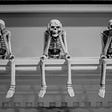 Three skeletons are sitting on a ledge; one covers its eyes, one its mouth and one its (non-existent) ears.