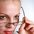 close up portrait of blonde woman pulling down her reading glasses to look over them