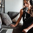 A female podcaster speaking to her laptop using a microphone.