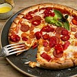 pepperoni pizza on plate with slice missing and fork on side three-bite rule