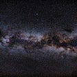 A picture of the starry sky from space. Dark blues, light and dark purples, golds, browns, and spots of white dot the sky.