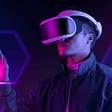A man is wearing a virtural reality headset as he reaches out with one finger. There is a neon pink hue over the man.