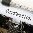 Image is a closeup of an older typewriter that had a ribbon and keys that struck it. A page of white paper is in the roller with the one word “Perfection” typed on it.
