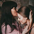 Woman in black hair kissing younger woman on forehead.