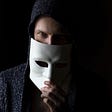A man wearing a hood looking over the top of a white mask.