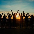 A group of people in front of a sunset cheering
