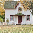 Picture of two story home with a white picket fence in front of it. The fence parts in front of the door. The House has a gray roof. The door and accents around the windows are maroon. There are windows on either side of the door and above the door. It colors of nature in the photo suggest it is summer.