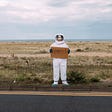 An astronaut in his spacesuit standing at the side of the road, acting as a hitchhiker who’s asking for a passage to Mars