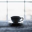A cup and saucer on a wooden table in front of a window.