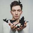 surreal image of young white male with brown hair in a long sleeve white shirt holding black butterflies coming out of his hands