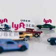 Toy cars with Uber and Lyft signs on top, arranged on a shiny white surface with a white background.
