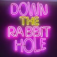 A pink and yellow neon sign that says “Down the rabbit hole.”