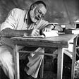 A black and white image of Ernest Hemingway writing on a notepad.