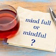 Glass of tea and pen next to napkin with text: “mind full or mindful?”