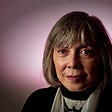 Image description: A middle aged lady with a bob cut, Anne Rice, smiling, with a purple background.