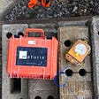 A Maturix Sensor and its case are laying next to each other on concrete blocks in a worksite.