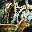 Large circular antique gears with big teeth, pale blue/teal in color, with patchy rust giving off the old/antiquey vibe.
