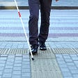 A blind person with a white cane navigates a city crosswalk