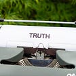 An old electric typewriter containing paper with the word “TRUTH.”