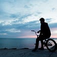 Man sittiung on bicycle next to a lake.