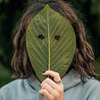 Woman hiding her face behind a leaf with two eyeholes