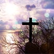 The image of a cross by a lake in the setting sun