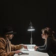 a male detective questioning a female suspect in a dark room with a table light.