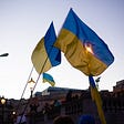 Image of two Ukraine flags waving during a public demonstration.