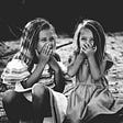 black & white photo of two young girls laughing with their hands over their mouths