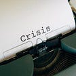 An antique typewriter, with a sheet of paper, having the word Crisis written on it.