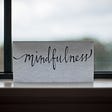 A paper with the word Mindfulness written on it, placed on a window ledge with a blurred background of a landscape.