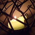 white candle burned down sitting in a dark wooden, circular cage.