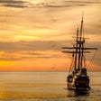 Image of a traditional ship sailing into the sunset.