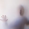 Human figure behind an opaque curtain with hands and mouth leaning against it